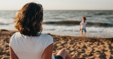 woman watching child playing on beach during daytime